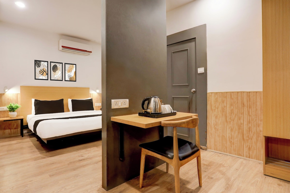 Una habitación de hotel con cama, mesita de noche, silla, escritorio y una puerta.