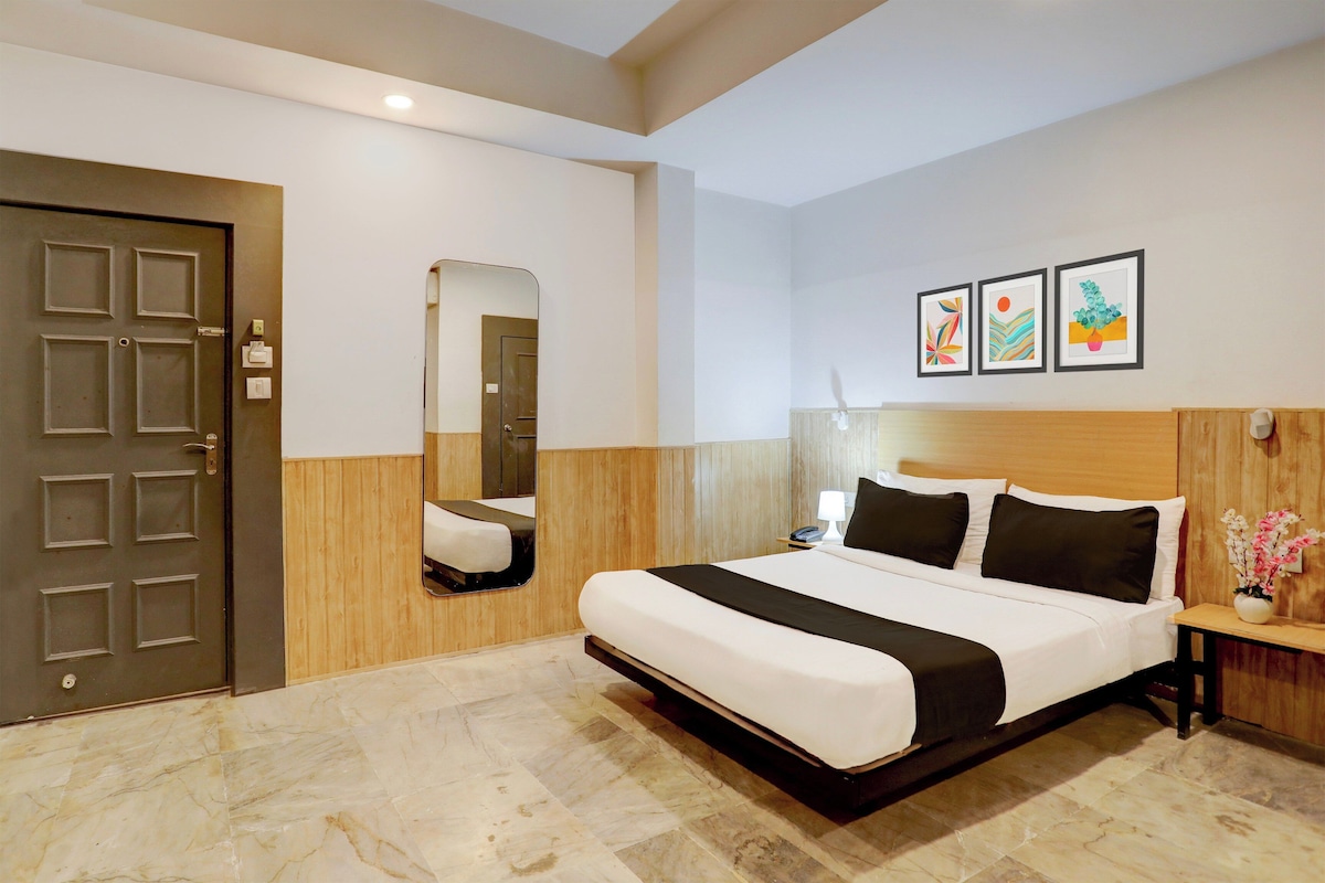 Habitación de hotel con cama, cabecera de madera, mesita de noche, espejo y tres cuadros en la pared.