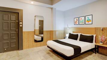 A hotel room with a bed, a wooden headboard, a nightstand, a mirror, and three framed artworks on the wall.