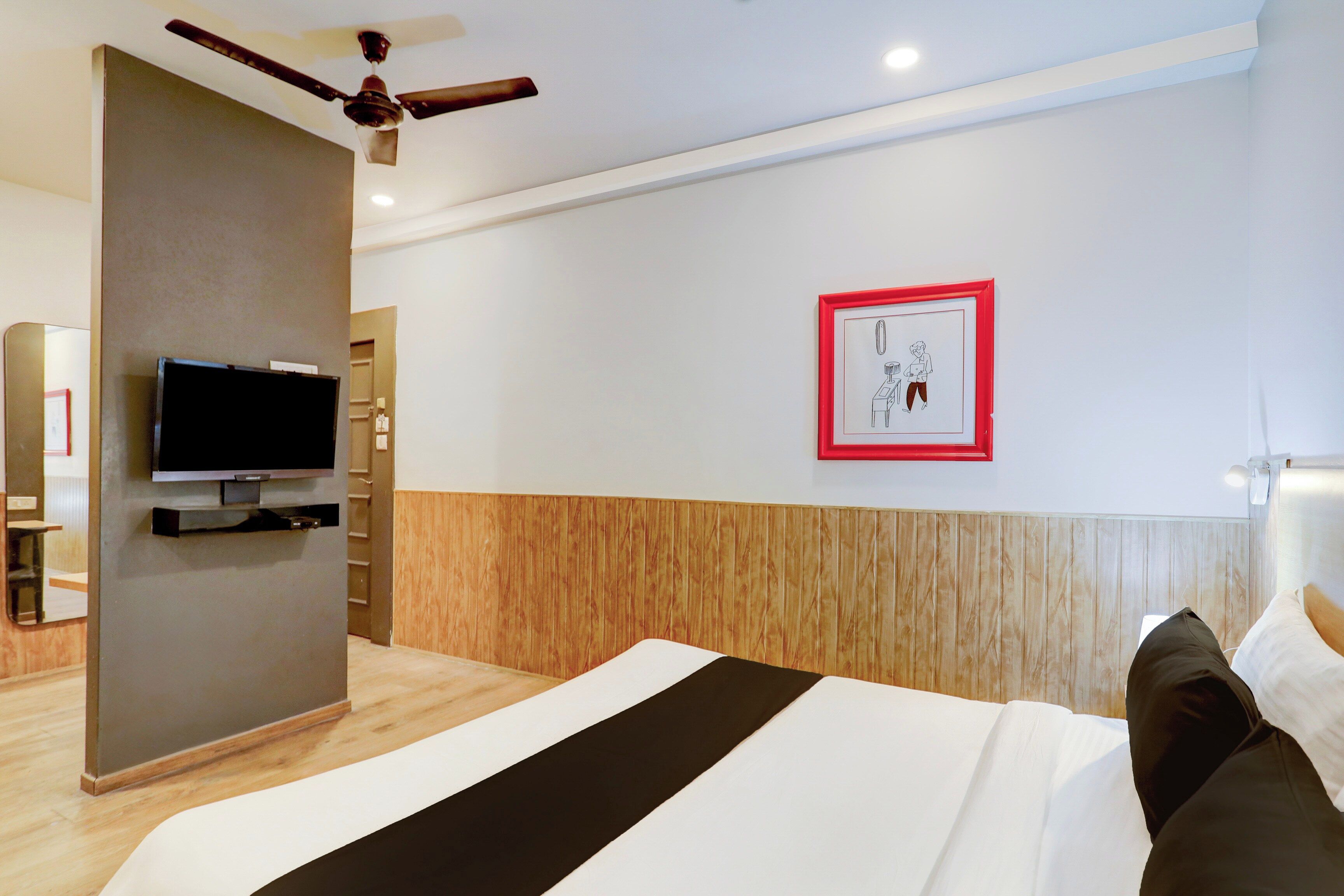 A hotel room with a bed, a television, a ceiling fan, a wooden panel wall, and a framed picture.