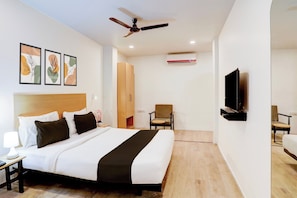 A hotel room with a bed, a desk, a chair, a television, and a ceiling fan. - Townhouse Kalmana (Nagpur)