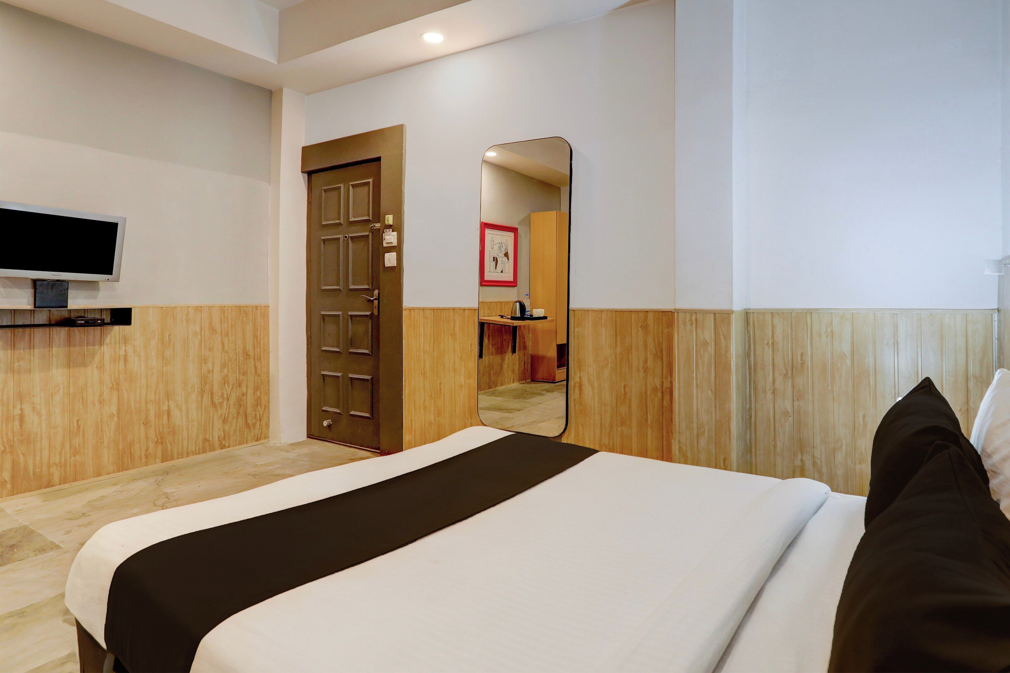 A hotel room with a bed, a television mounted on the wall, a door, and a mirror.