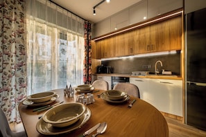 A modern kitchen with wooden cabinets, a stainless steel refrigerator, and a dining table set with plates and cutlery. - RentPlanet - Apartamenty Wilkaska (Wrocław)