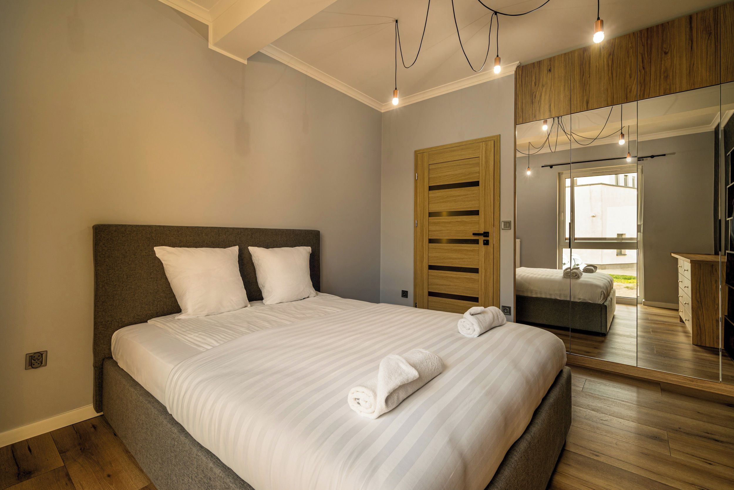 A modern bedroom with a large bed, wooden headboard, and a mirror cabinet.