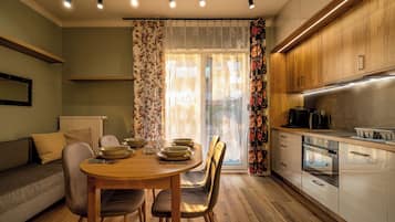 A modern kitchen with wooden cabinets, a dining area with a table and chairs, and a window with floral curtains.
