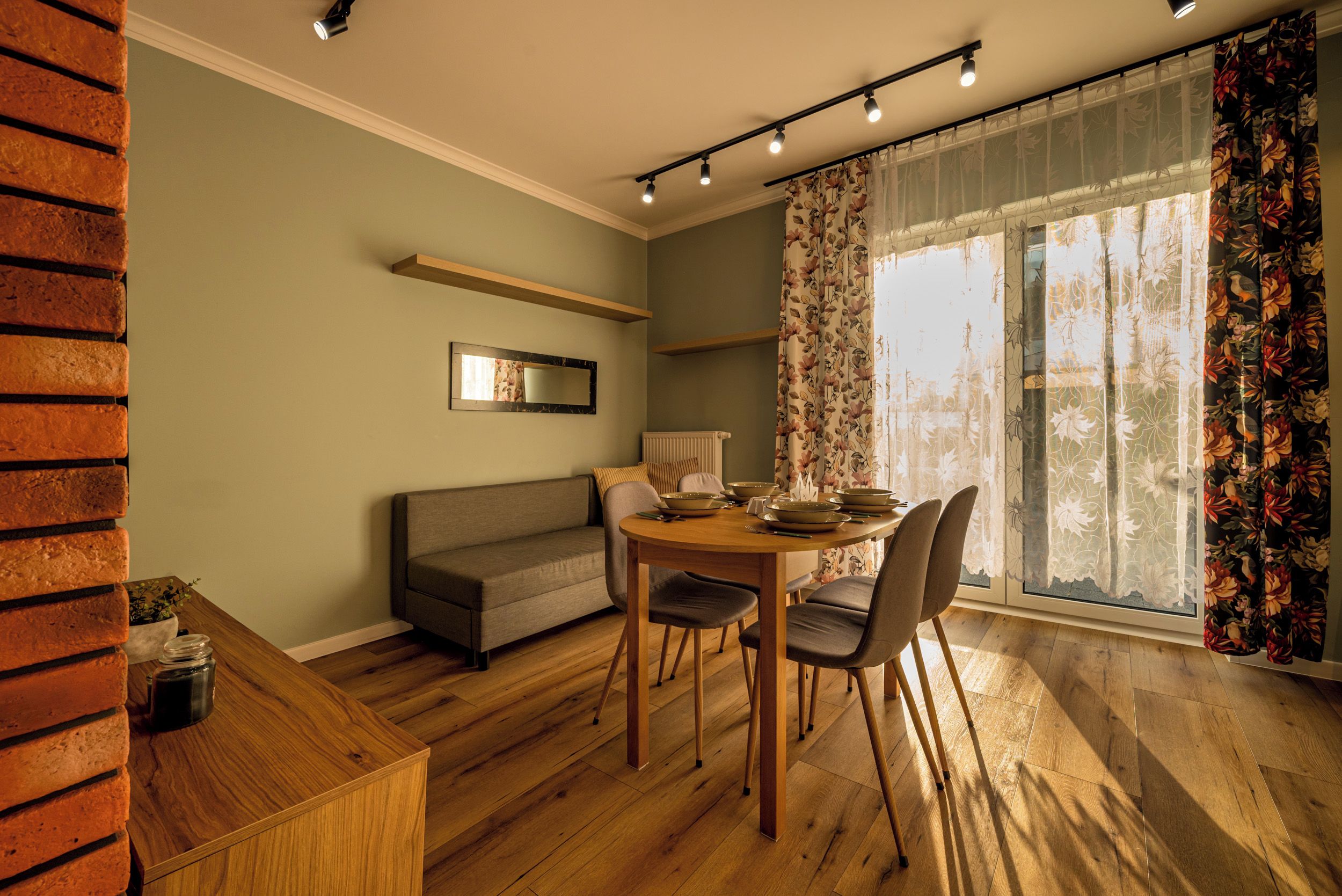 A room with a dining table, chairs, a sofa, a mirror, and a window with curtains.