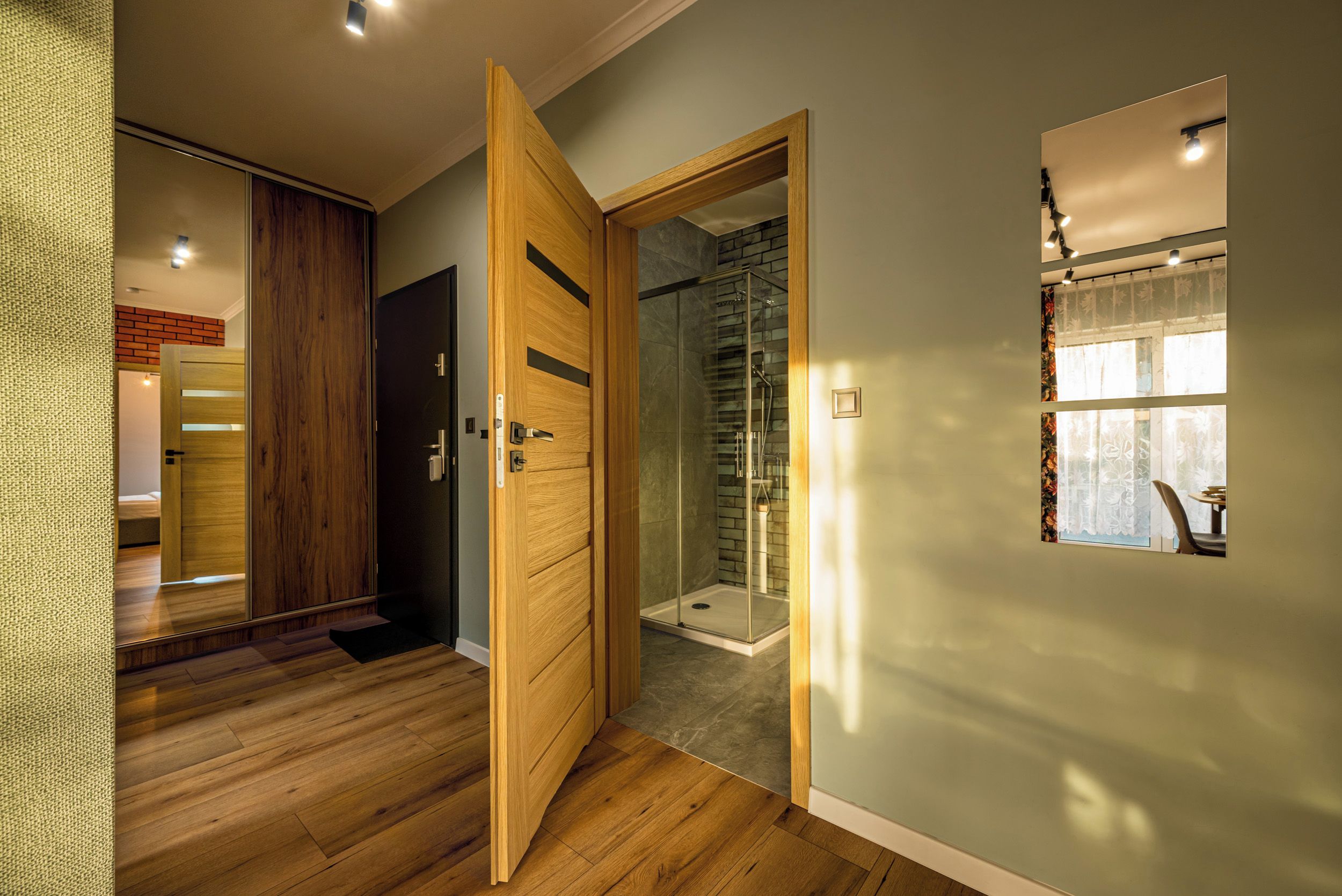 A modern bathroom with a glass shower enclosure, wooden flooring, and a visible showerhead.