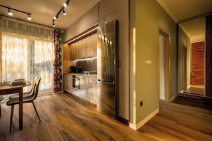 A modern kitchen with a stainless steel refrigerator, wooden cabinets, and a dining area with a table and chairs. - RentPlanet - Apartamenty Wilkaska (Wrocław)