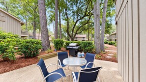 An outdoor patio with a round table and chairs, surrounded by trees and a barbecue grill. - 2-Bedroom 2.5-Bathroom villa located on Hilton Head Island! (Hilton Head)