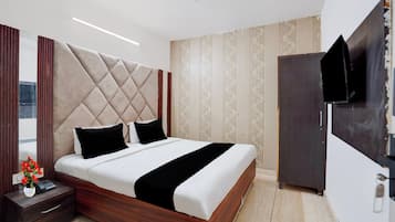 A modern bedroom with a tufted headboard, a wooden bed frame, a bedside table with a vase of flowers, and a TV mounted on the wall.