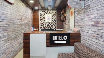 A hotel reception desk with a wooden counter, a sign reading 'HOTEL OYO-Serviced', and a patterned wall behind it.