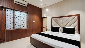 Quarto com cama, painéis de madeira, janela com padrão de poços e um aparelho de ar condicionado.