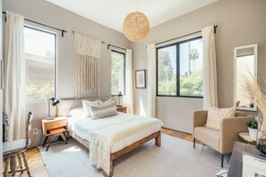 A spacious bedroom with a large bed, a chair, a desk, and a hanging light fixture. - Jacaranda House | Designer Retreat with Private Hot Tub (Venice, Los Angeles)