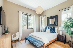 Une chambre à coucher avec un grand lit, des tables de chevet, un bureau, une chaise et un luminaire suspendu.