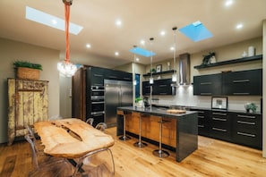 A modern kitchen with dark cabinetry, stainless steel appliances, and a central island. - Jacaranda House | Designer Retreat with Private Hot Tub (Venice, Los Angeles)