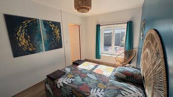 Ein Schlafzimmer mit einem Bett, einem Sessel, einem Fenster mit Vorhängen und Bildern an der Wand.