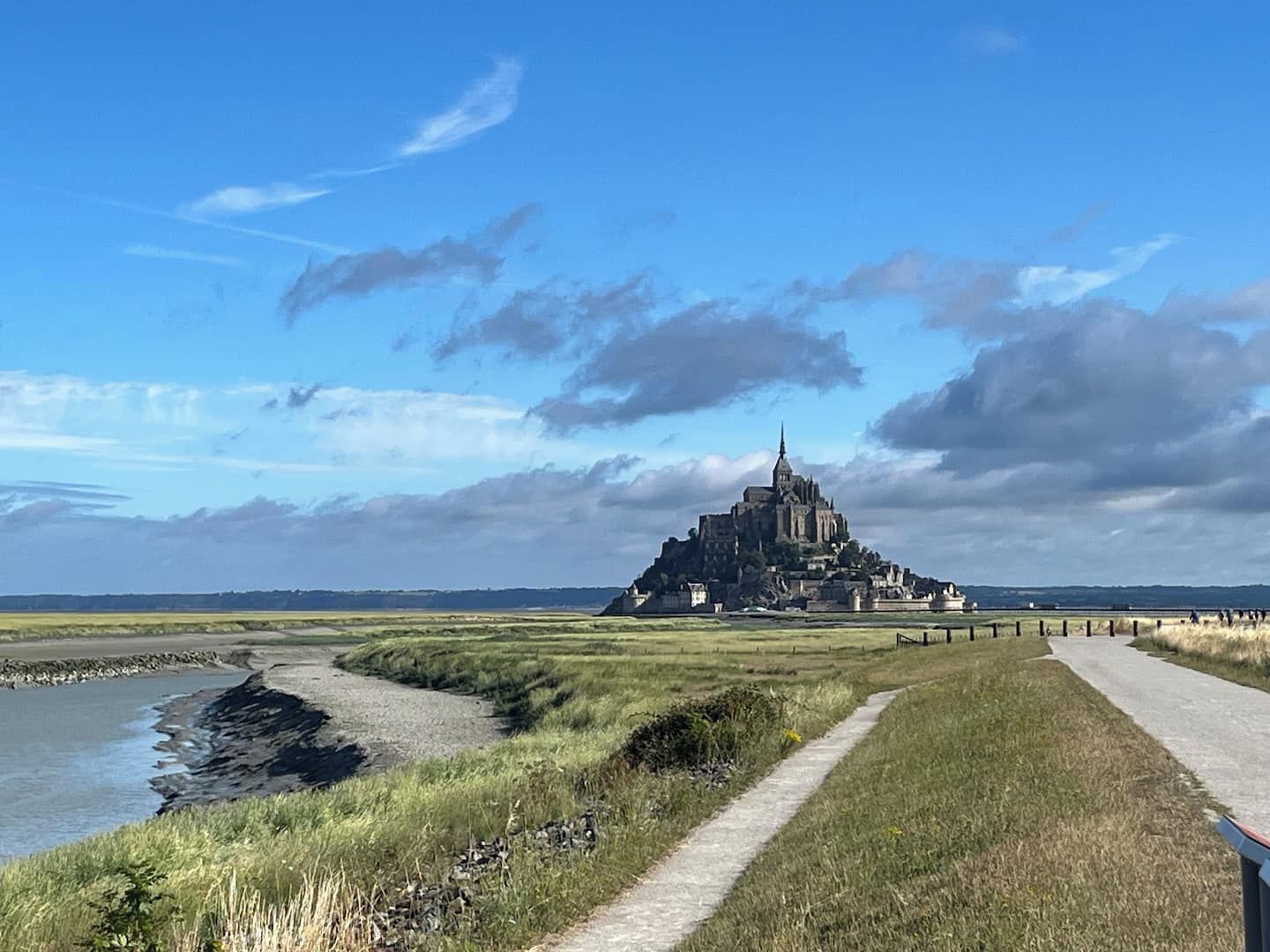 Un sentier côtier mène à un château historique, reconnaissable à son imposante tour, qui est entouré de prairies verdoyantes et surplombé par un ciel dégagé.