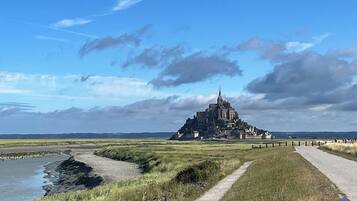 Un sentier côtier mène à un château historique, reconnaissable à son imposante tour, qui est entouré de prairies verdoyantes et surplombé par un ciel dégagé.