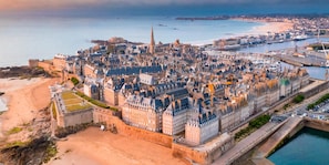 A coastal cityscape with historic architecture, a prominent church spire, and a fortified wall.