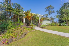 Uma casa com varanda coberta, rodeada por um jardim bem cuidado e diversas plantas.