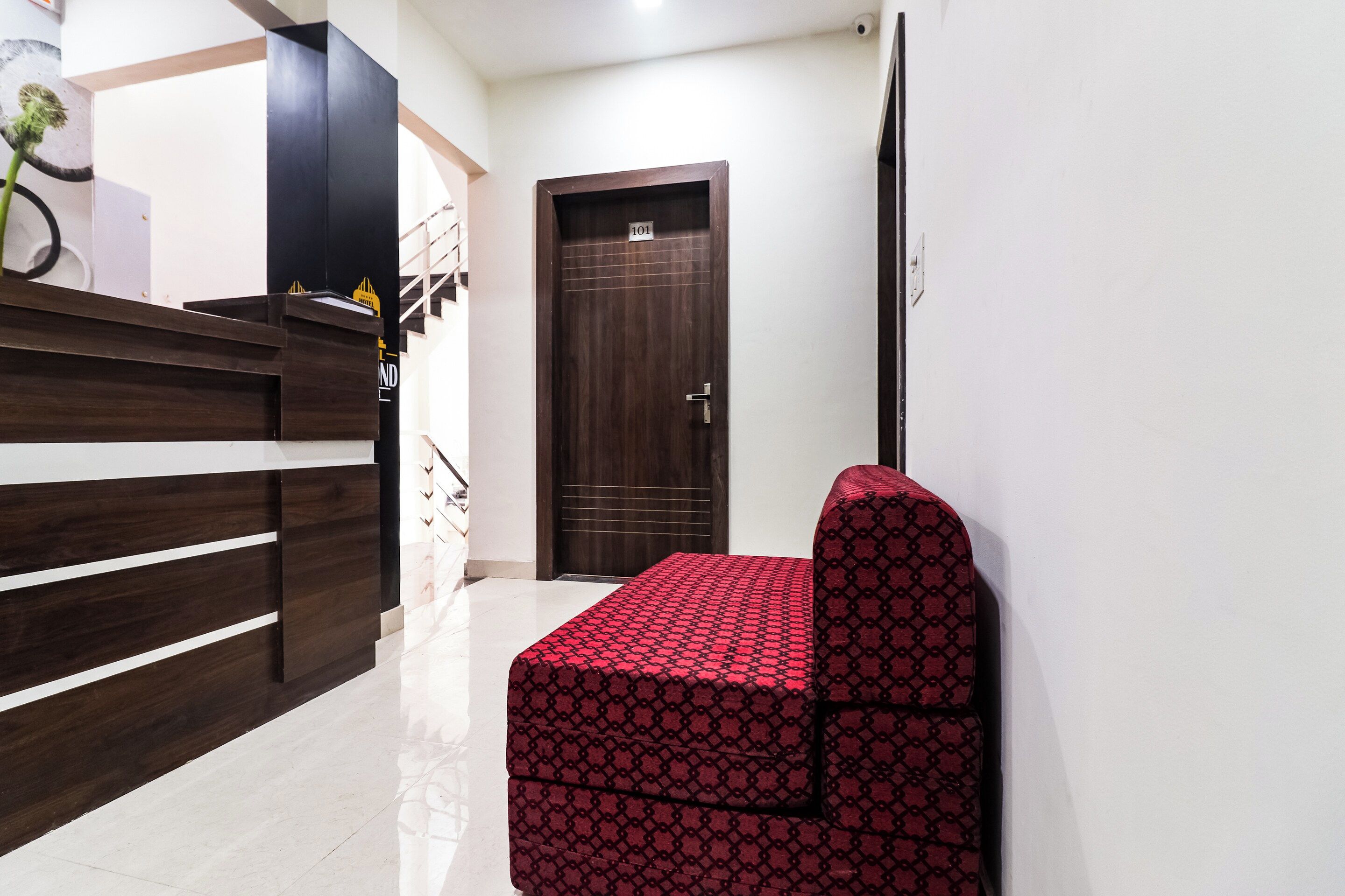 A hotel reception area with a reception desk, a wooden counter, a dark wooden door, and a red patterned bench.