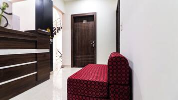 A hotel reception area with a reception desk, a wooden counter, a dark wooden door, and a red patterned bench.