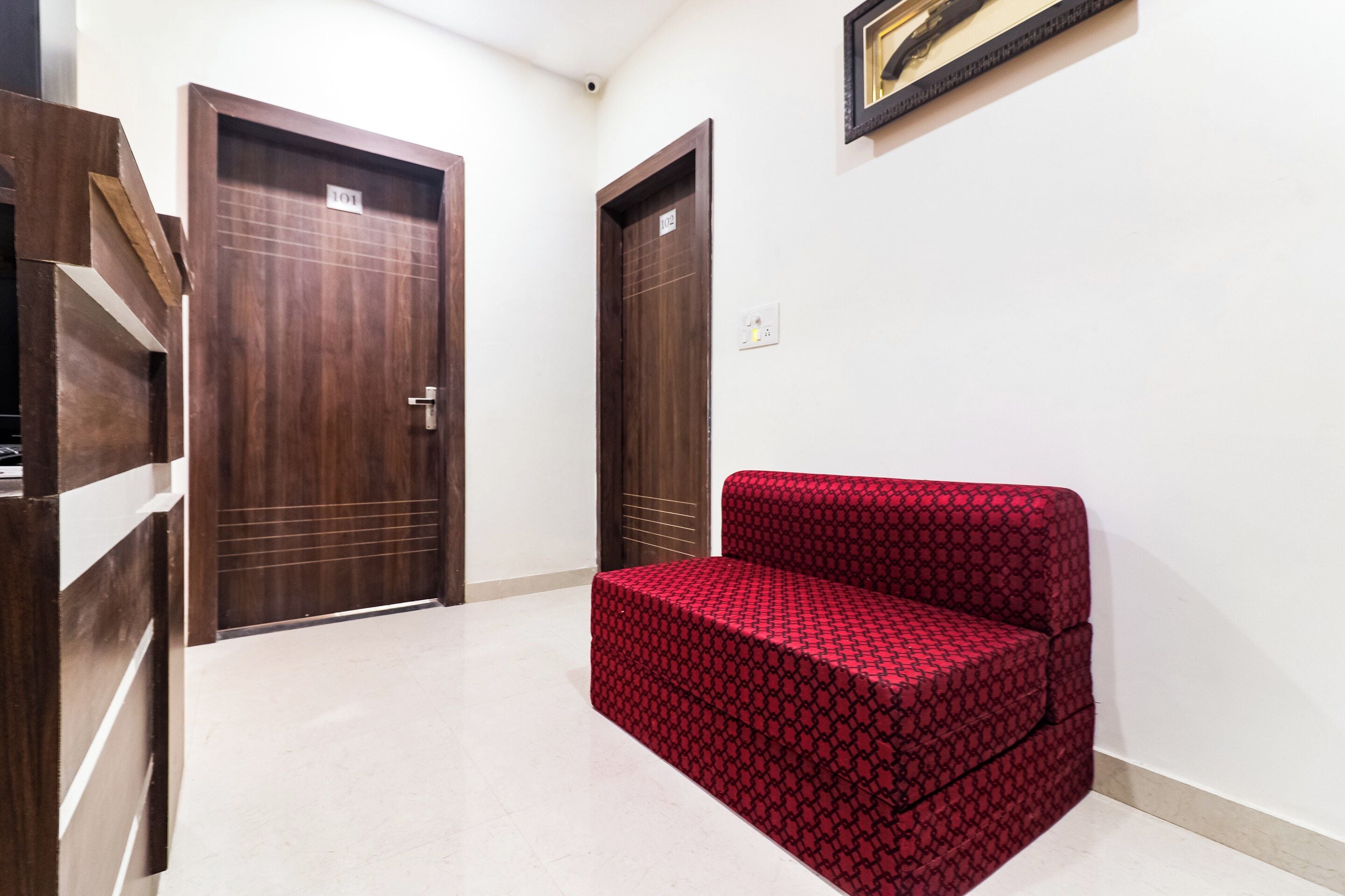 A hallway with two wooden doors, one labeled '101' and the other '102', and a red patterned sofa in the center.