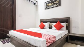 A hotel room with a bed, a nightstand, a wall-mounted air conditioner, and a framed picture.