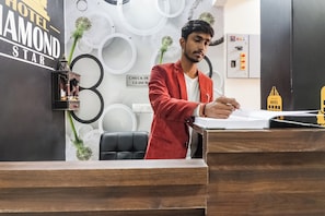 Un mostrador de recepción de hotel con un cartel de registro, un reloj y una pequeña maqueta del edificio del hotel.
