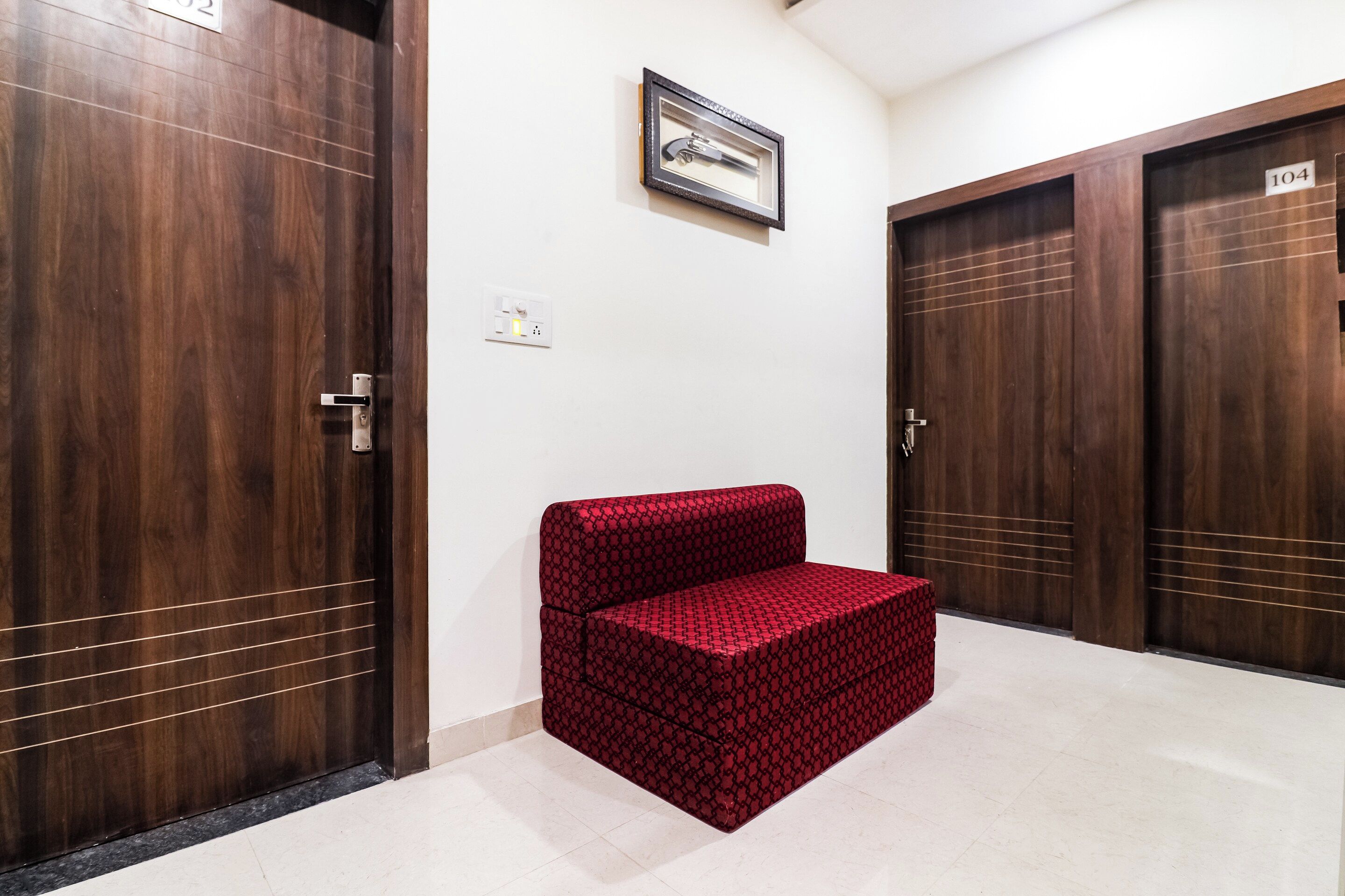 A hallway with wooden doors, a red patterned bench, and a framed picture on the wall.