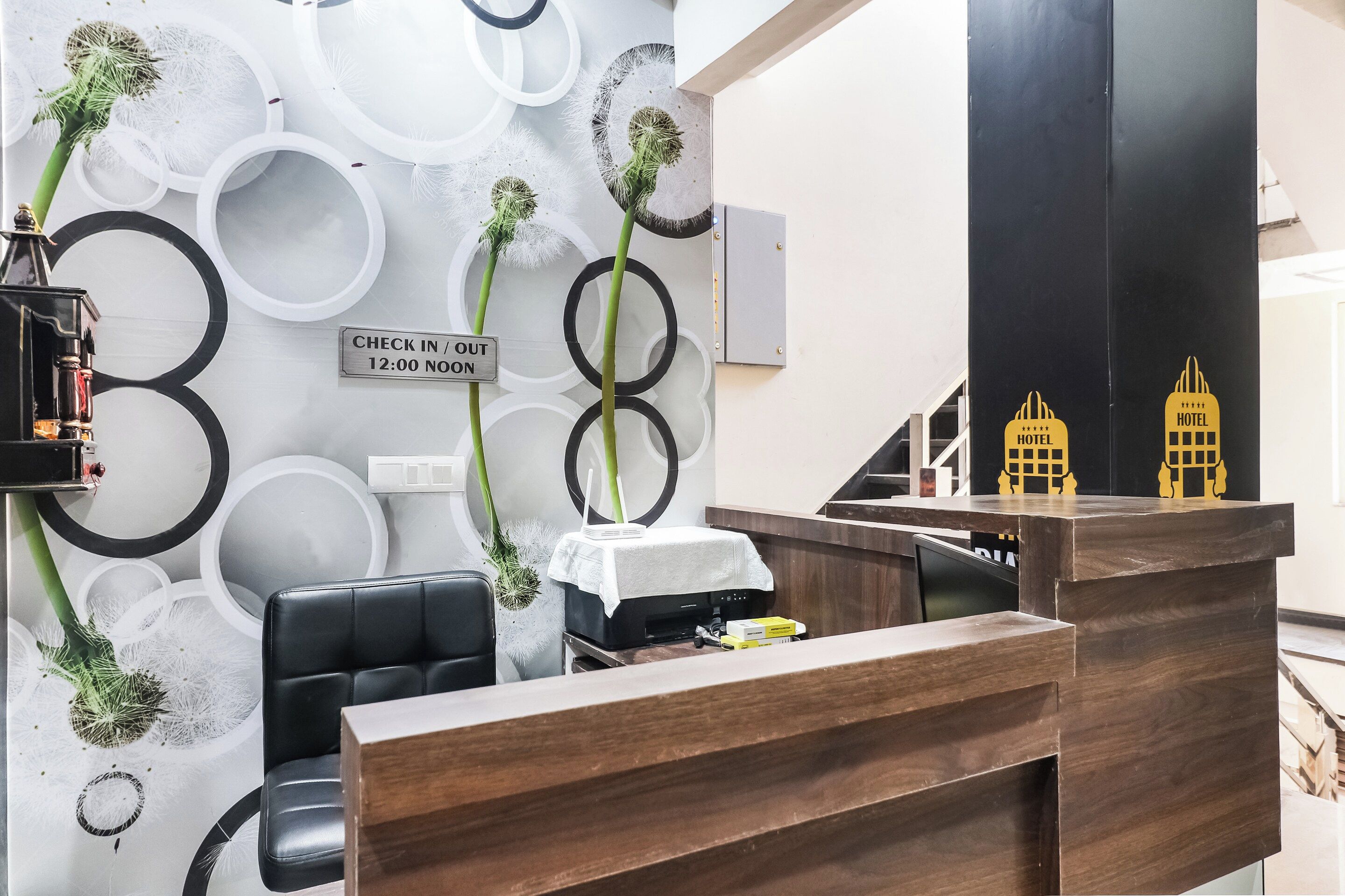A hotel reception desk with a check-in/out sign, a black leather chair, and a small table with a white cloth.
