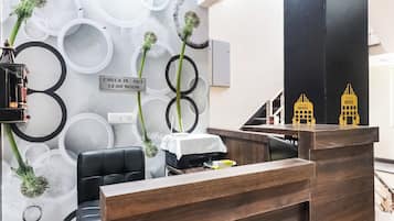 A hotel reception desk with a check-in/out sign, a black leather chair, and a small table with a white cloth.