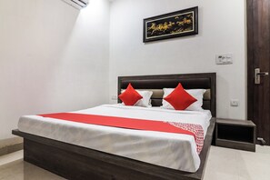 A hotel room with a bed, a nightstand, a door, and a wall-mounted light switch.