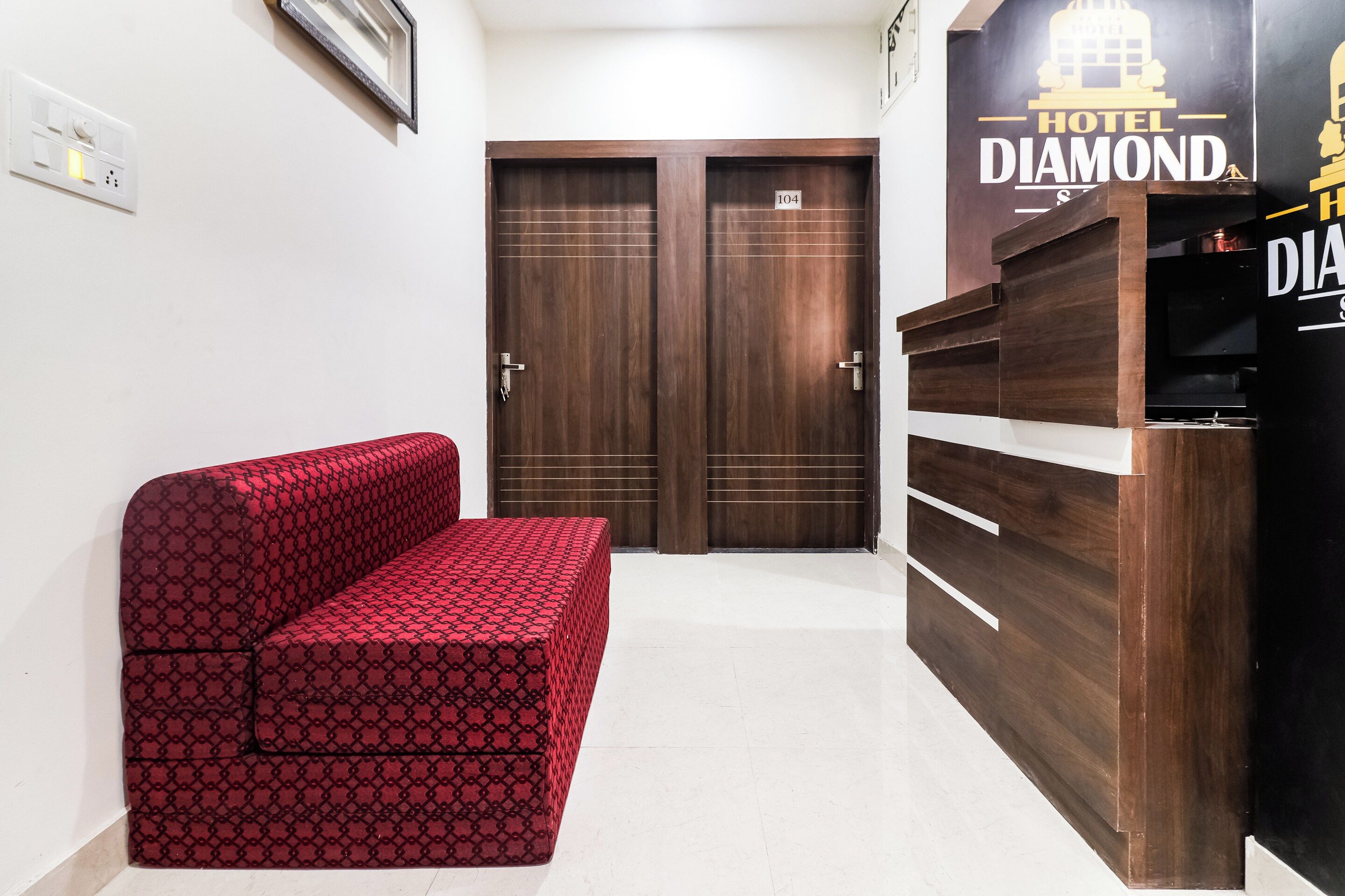 A hotel room with a red patterned sofa, a wooden wardrobe, and a door marked with the number 104.