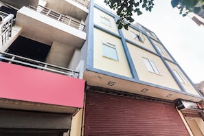 Un edificio de varios pisos con una planta baja de persianas rojas, balcones en los pisos superiores y un ventanal visible en el segundo piso.