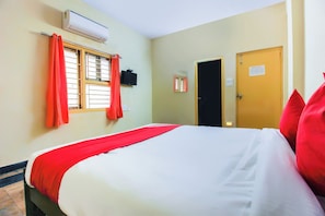 A hotel room with a bed, a window with curtains, an air conditioning unit, a door, and a wall-mounted TV. - Hotel O Sai Residency (Hyderabad)