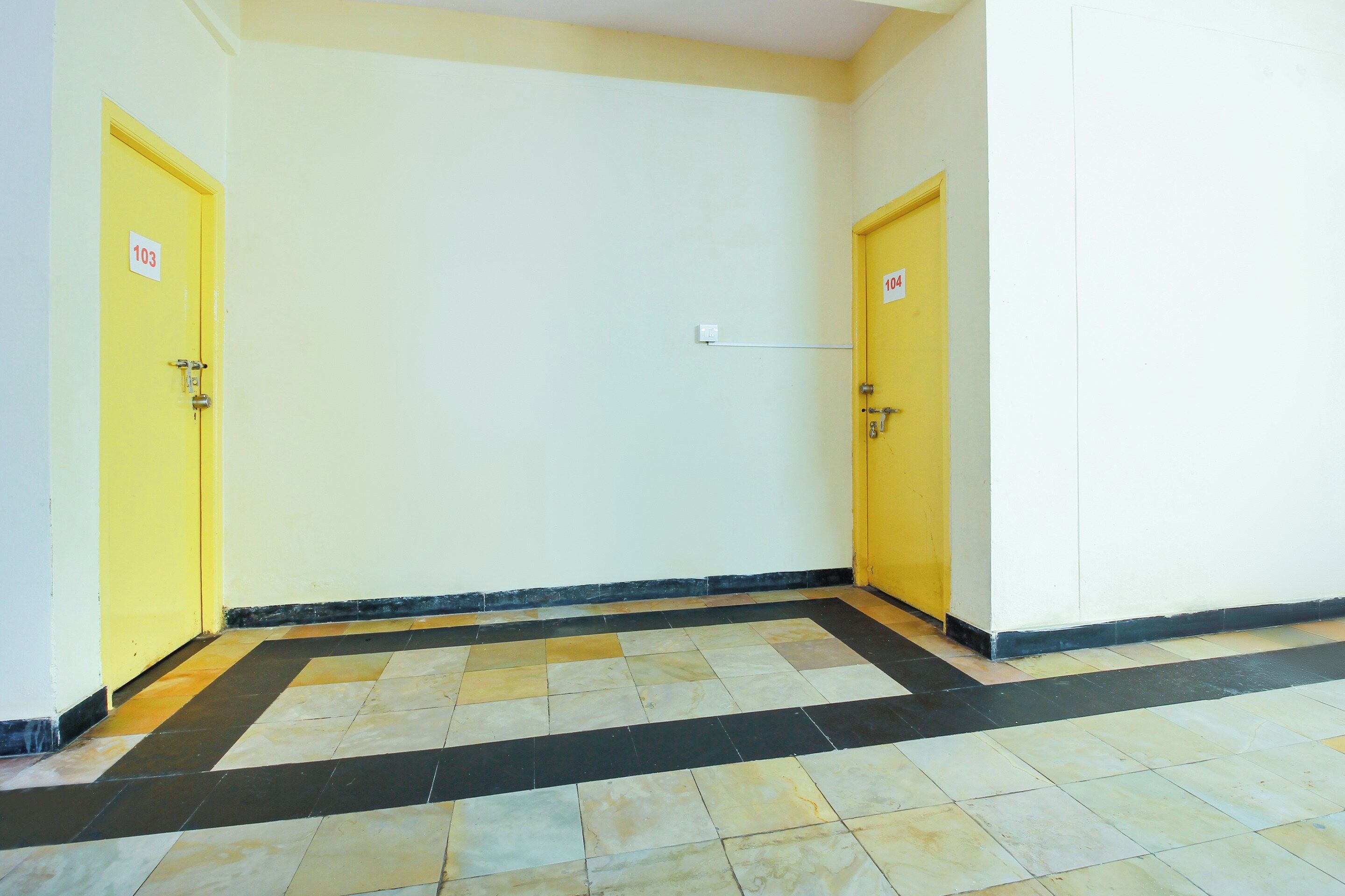 A hallway with two yellow doors, each marked with a number. The floor is tiled with a black and beige pattern.