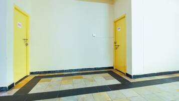 A hallway with two yellow doors, each marked with a number. The floor is tiled with a black and beige pattern.