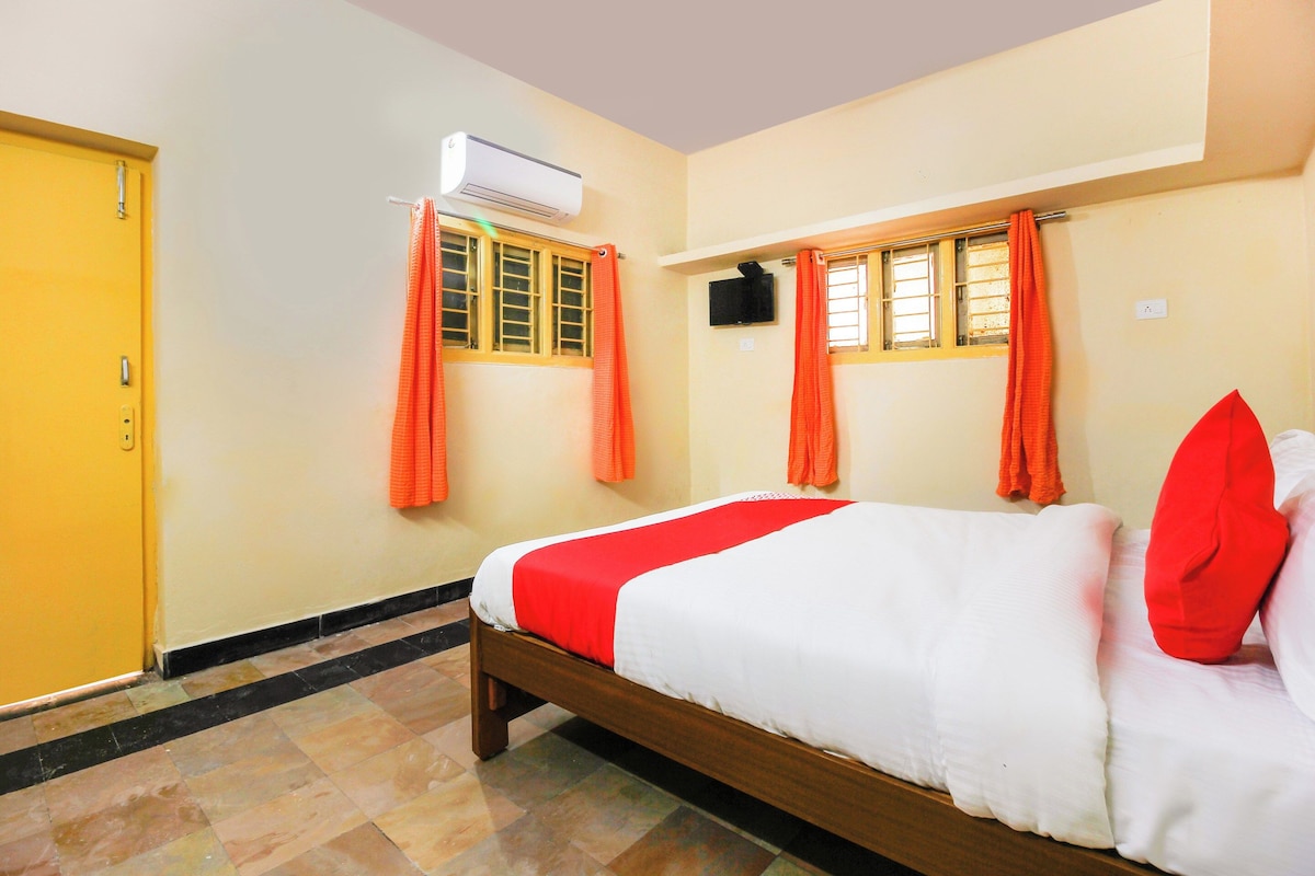 A hotel room with a bed, an air conditioning unit, a television, and orange curtains.
