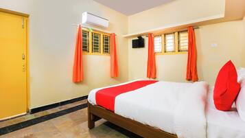 Une chambre d’hôtel avec un lit, un appareil de climatisation, une télévision et des rideaux orange.