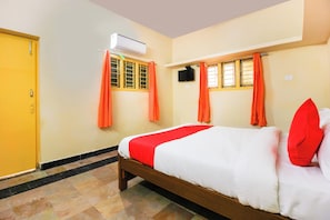 A hotel room with a bed, an air conditioning unit, a television, and orange curtains. - Hotel O Sai Residency (Hyderabad)