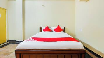 A neatly made bed with a wooden headboard, white bedding, and red pillows.