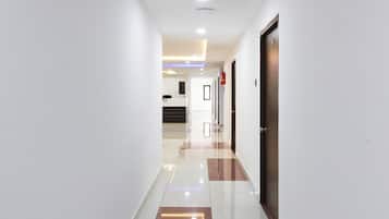 Un pasillo de hotel con diseño moderno, que presenta una combinación de piso de baldosas blancas y marrones, paredes blancas y una puerta de madera a la derecha.