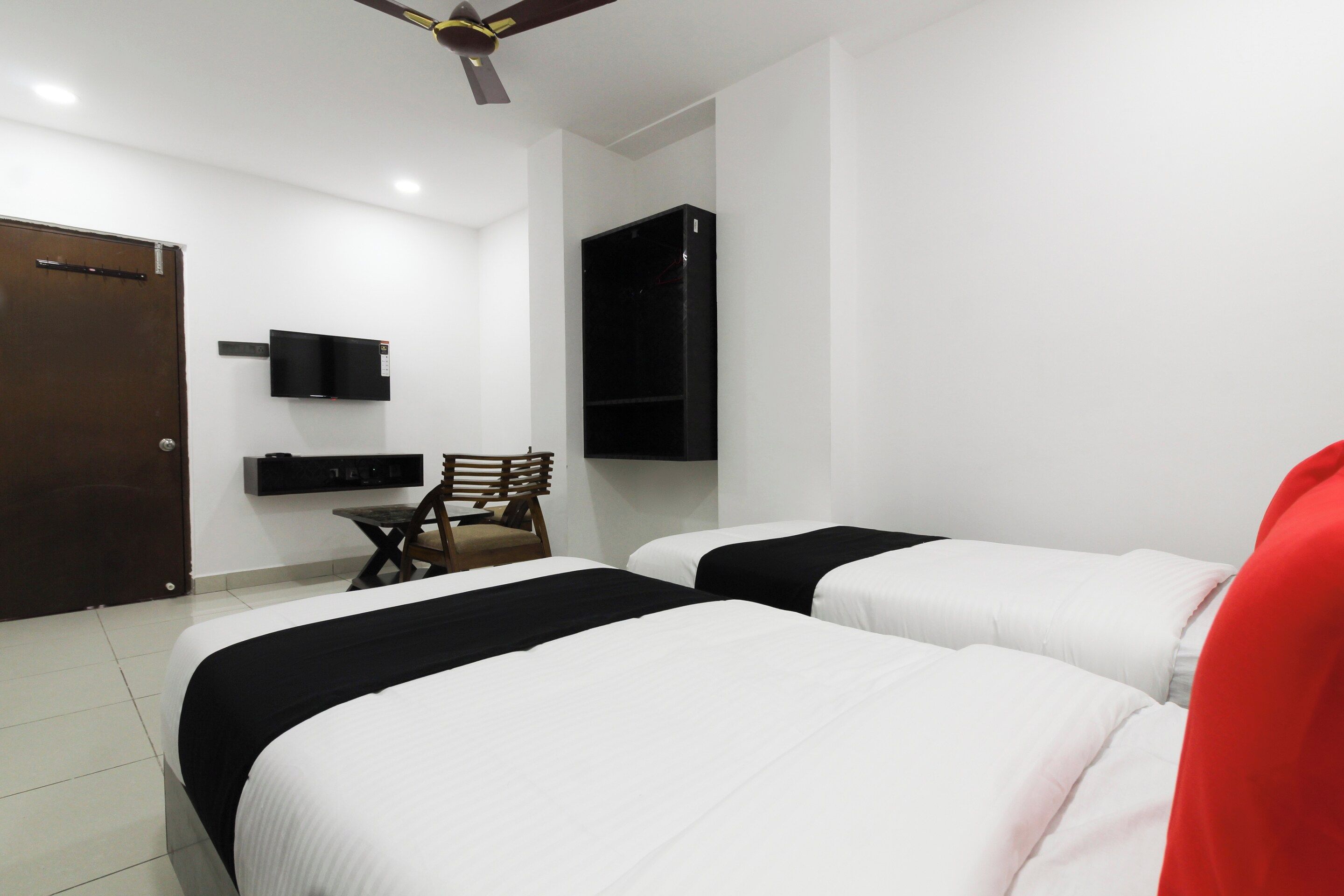 Habitación de hotel con dos camas, un escritorio, una silla, televisor montado en la pared y un ventilador de techo.