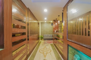 A corridor with wooden paneling, a stone wall, a patterned rug, and a reception desk with a plant. - Hotel O Meredian comfort inn (Hyderabad)