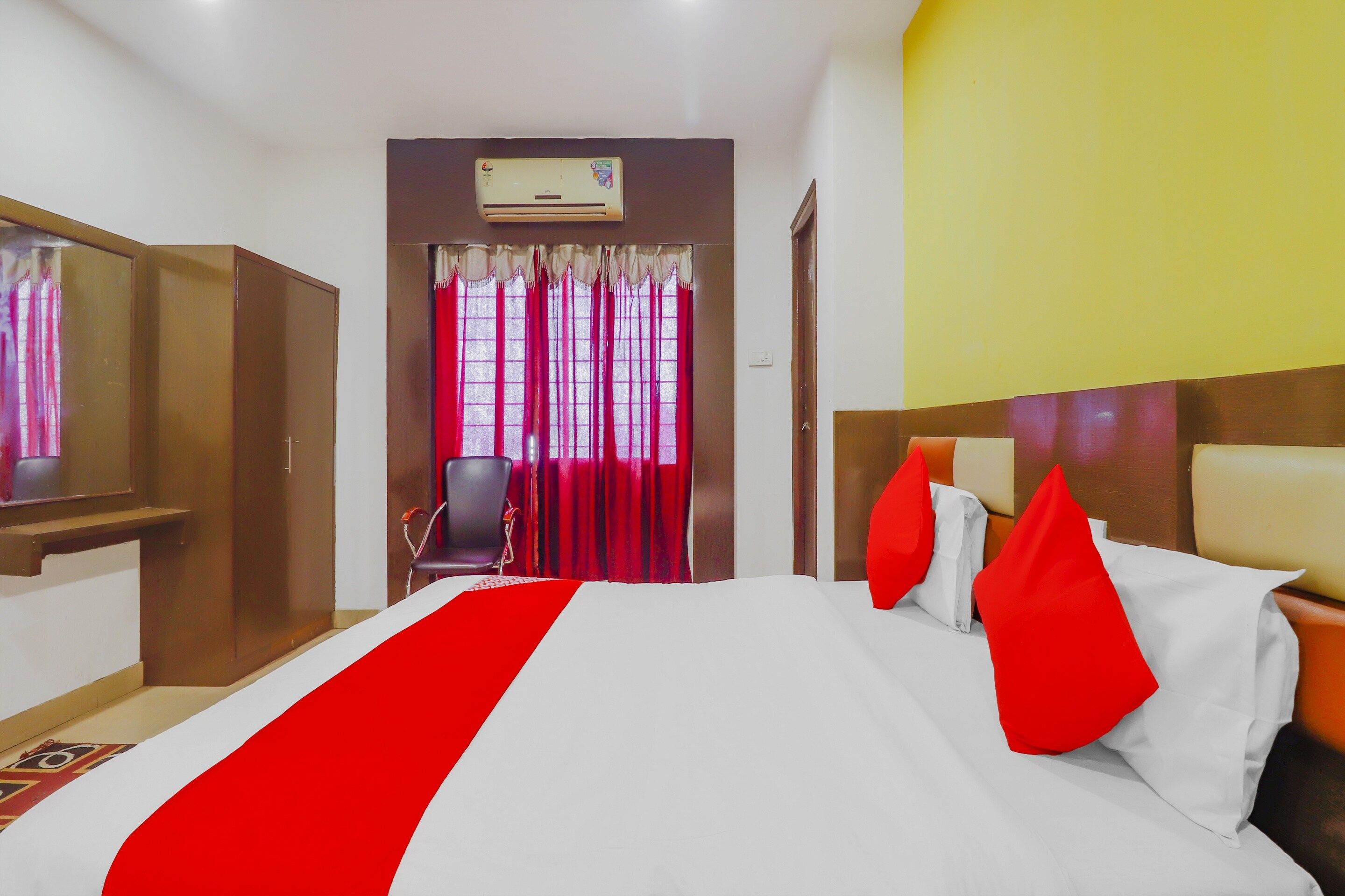 A hotel room with a bed, a desk, a chair, a wardrobe, and an air conditioning unit.