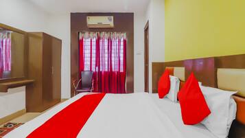 Habitación de hotel con cama, escritorio, silla, armario y aire acondicionado.