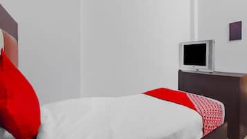 Una habitación de hotel con una cama, un televisor sobre un soporte y una mesita.