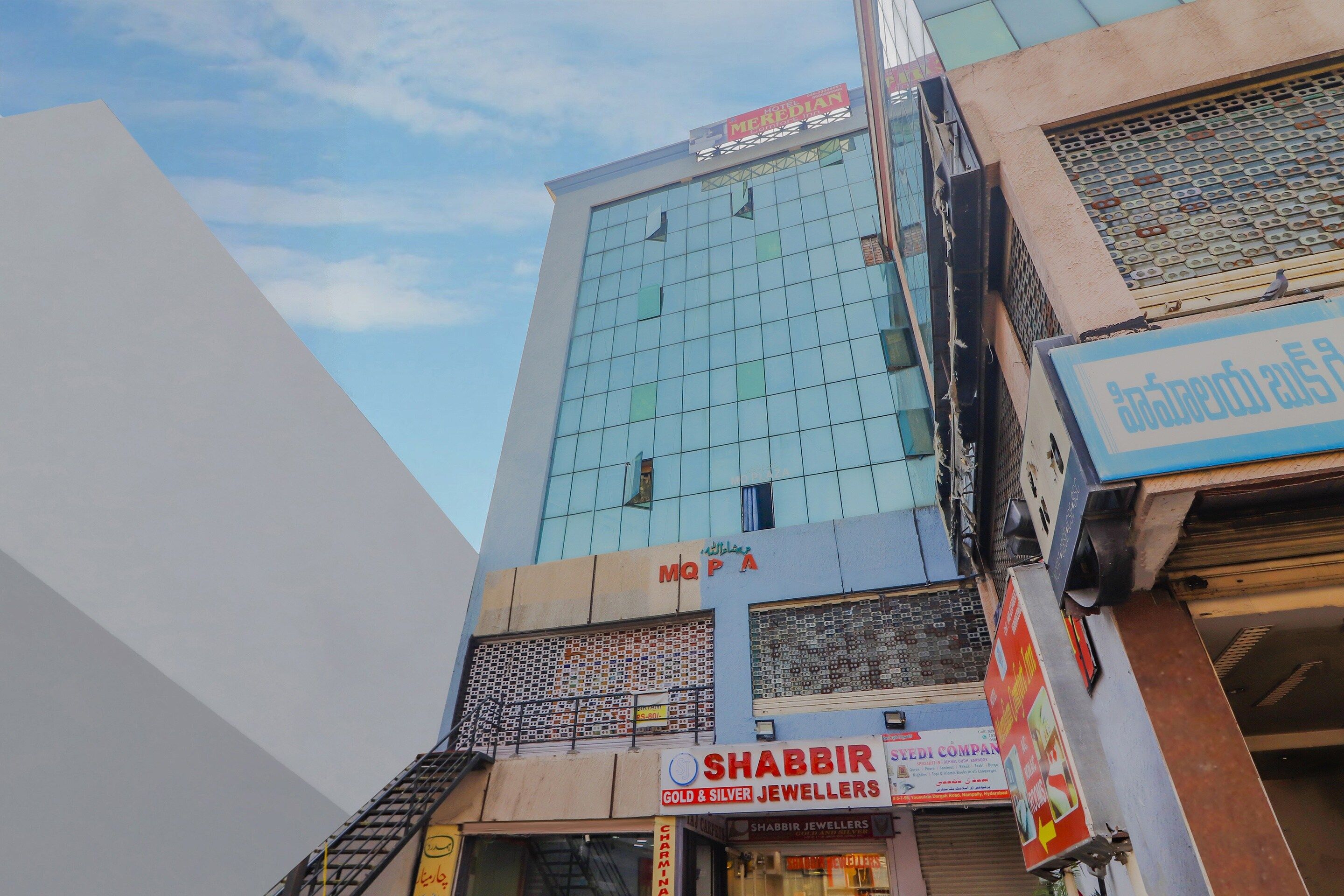 A multi-story building with a modern glass facade, a visible sign for 'Hotel Meredian', and a storefront for 'Shabbir Gold & Silver Jewellers'.