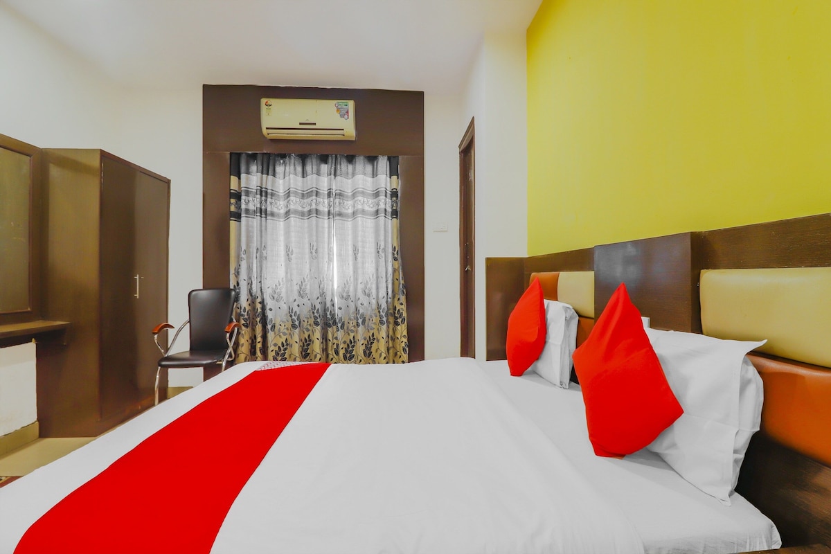 A hotel room with a bed, a chair, a TV, and a window with curtains.